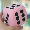 A hand holding a large pink die with black dots. Produktbild-Vorschau