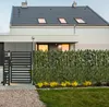 A modern house with a black gate and a green leaf-covered fence in front of it. Anteprima dell’immagine prodotto