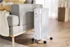 A white oil-filled radiator is placed on a wooden floor next to a grey sofa with a knitted blanket and yellow cushions. Produktbild-Vorschau