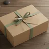 A brown cardboard gift box with a green ribbon and a gift tag, placed on a wooden surface. Podgląd zdjęcia produktu