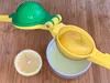A manual citrus juicer with a lemon half and a bowl of lemon juice. Produktbild-Vorschau