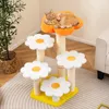 A cat is resting on a multi-tiered cat tree designed to look like flowers, placed in a room with a plant and furniture. Podgląd zdjęcia produktu