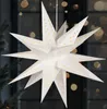 A white paper star lantern with gold star cutouts hangs in front of a dark background with bokeh lights. Podgląd zdjęcia produktu