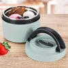 A mint green insulated food container filled with scoops of ice cream and berries, with its lid open and placed beside it on a wooden table. A strawberry is also visible on the table. Náhled obrázku produktu