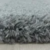 A close-up, low-angle view of a shaggy, high-pile gray rug with a light wood floor visible underneath. Produktbild-Vorschau