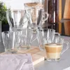 A set of clear glass mugs, one filled with a layered coffee drink, arranged on a wooden board on a countertop. Voir les images du produit