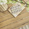 A close-up of a patterned card on a wooden table, with a vase and flowers in the background. Produktbild-Vorschau
