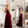 A woman is posing in front of a full-length mirror in a room with clothing racks and shelves. Produktbild-Vorschau