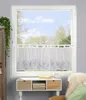A window with a sheer curtain featuring a lavender pattern, above a small white cabinet with wooden drawers. Produktbild-Vorschau