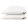 Two white pillows are stacked on top of each other against a white background. Each pillow has an orange trim and a small black and gray tag with a white 'M' logo on the right side. Anteprima dell’immagine prodotto