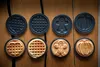 Various waffle plates and freshly made waffles in different shapes, placed on a wooden surface. Podgląd zdjęcia produktu