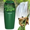 A green reptile water feature with plants and water flowing, set against a backdrop of a waterfall and lush greenery, with a frog perched on a leaf in the foreground. Voir les images du produit