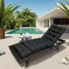 A black lounge cushion is placed on a patio next to a swimming pool, with palm trees and a modern house in the background. Náhled obrázku produktu