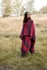 A woman stands in a field wearing a poncho and skirt. Produktbild-Vorschau