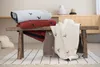 Several folded blankets with deer patterns are displayed on a rustic wooden bench, placed on a striped rug in a room with wooden furniture in the background. Produktbild-Vorschau