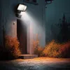 A solar-powered LED floodlight illuminates a doorway at night, with surrounding bushes and foliage lit by the light. Produktbild-Vorschau