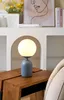 A blue and white table lamp sits on a wooden side table next to a couch. Podgląd zdjęcia produktu
