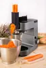 A kitchen machine is shown grating carrots into a metal bowl, with whole carrots on a cutting board in the foreground. Podgląd zdjęcia produktu