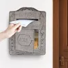 A hand is inserting a letter into a vintage-style metal mailbox mounted on a white wall next to a brown door. Podgląd zdjęcia produktu