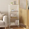 A white metal shelf unit with light wood-colored shelves is placed next to a beige sofa. The shelves contain decorative items and books. Produktbild-Vorschau