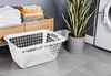 A white laundry basket is placed on a tiled floor in a laundry room, next to a washing machine and a potted plant. Produktbild-Vorschau