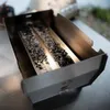 A close-up shot of a stainless steel smoking tray filled with dark, granular material. Produktbild-Vorschau