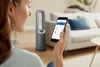 A woman using a smartphone to control a smart fan in a living room. Podgląd zdjęcia produktu