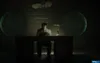 A man sits at a desk in a dimly lit room, typing on a typewriter. The room has wooden walls and two large, circular objects on the walls. Podgląd zdjęcia produktu