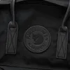 A close-up view of the Fjällräven Kånken logo on a black backpack. Produktbild-Vorschau