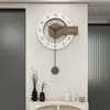 A modern wall clock with a pendulum hangs on a white wall above a console table with decorative vases. Produktbild-Vorschau