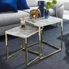 A set of nesting tables with marble-look tops and gold metal frames, placed on a dark carpet next to a sofa. Produktbild-Vorschau