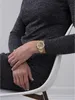 A person wearing a gold watch is sitting on a white chair. Náhľad obrázku produktu