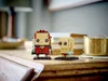 Two LEGO BrickHeadz figures, Frodo and Gollum, are displayed on a wooden surface with books and a brass pot in the background. Anteprima dell’immagine prodotto