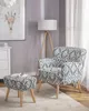 A living room scene with a patterned armchair and ottoman, a floor lamp, and a framed artwork. Náhled obrázku produktu