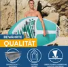 A man holding a paddleboard on a beach with rocks in the background. Produktbild-Vorschau