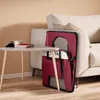 A dark red foldable dog crate is leaning against a light-colored sofa next to a small triangular table with a book on it. Anteprima dell’immagine prodotto