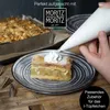 A slice of apple cake is being decorated with whipped cream from a piping bag, with a baking pan and piping tips visible. Anteprima dell’immagine prodotto