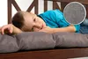 A young boy is lying on a cushioned bench, resting his head on his arms. A close-up inset shows the texture of the cushion fabric. Produktbild-Vorschau