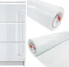A roll of white, high-gloss furniture film is shown next to a section of white, high-gloss furniture with drawers. Produktbild-Vorschau