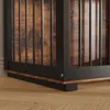 A close-up view of the bottom corner of a dog crate, showing the black metal frame and the wood-grain paneling. Produktbild-Vorschau