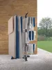 A drying rack with clothes is placed on a patio with a brick wall behind it and a grassy area with trees in the background. Voir les images du produit