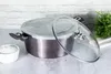 A pot with a glass lid is placed on a countertop, with a small bowl of white powder to the left and a green plant in the background. Produktbild-Vorschau