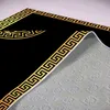A close-up, angled view of a black rug with a gold Greek key border, showing the underside of the rug. Produktbild-Vorschau