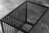 A close-up view of a modern coffee table with a black metal frame and a glass top, set against a dark, textured background. Produktbild-Vorschau
