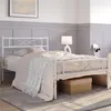 A white metal bed frame with a patterned headboard is shown in a bedroom setting. Podgląd zdjęcia produktu
