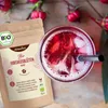 A bag of hibiscus flowers next to a glass of iced hibiscus tea. Produktbild-Vorschau