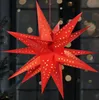 A red, star-shaped paper lantern with small gold stars cut out of it, hanging in front of a blurred background with bokeh lights. Náhled obrázku produktu