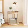 A round side table next to a bed, with a lamp, plant, and drinks on top, and a basket with clothes on the shelf below. Podgląd zdjęcia produktu