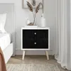 A bedside table with two black drawers and wooden legs, next to a bed and a curtain. Produktbild-Vorschau