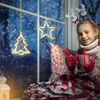 A young girl sits by a window at night, decorated with Christmas lights, wearing a festive sweater and mittens. Produktbild-Vorschau